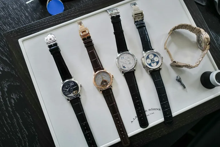 Four A. Lange & Söhne Handwerkskunst watches and a fifth watch on a gold bracelet, laid out on a white presentation tray