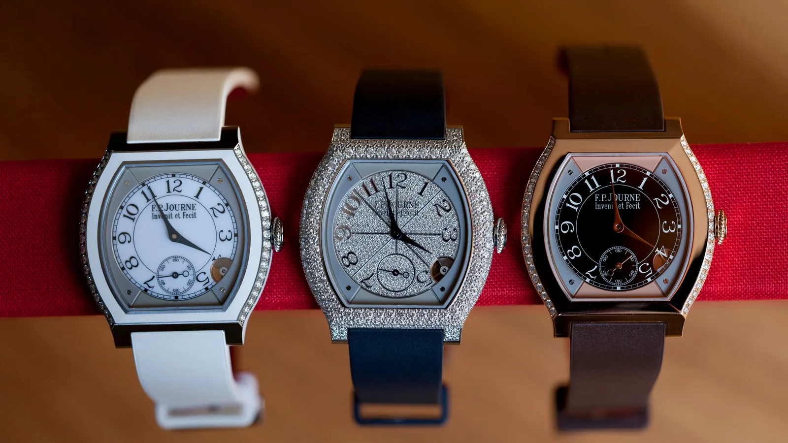 Three F.P. Journe Élégante watches with diamond-set tonneau cases, on white, navy and brown straps, displayed side by side