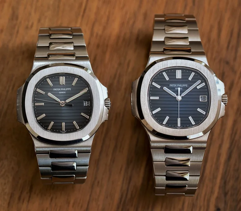 Patek Philippe Nautilus 5711/1A-010 in steel beside the 5811/1G-001 in white gold, both with blue dials and integrated bracelets, on a wooden surface