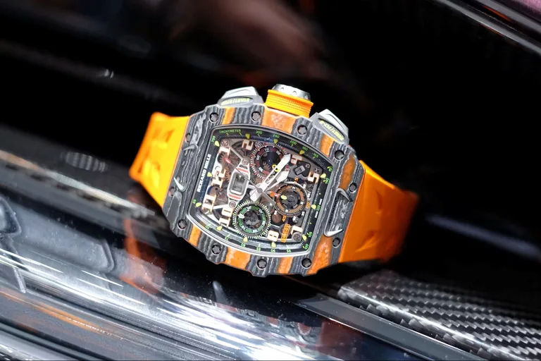 A Richard Mille RM 11-03 McLaren in Carbon TPT with orange Quartz TPT, on an orange rubber strap, resting on a black carbon surface